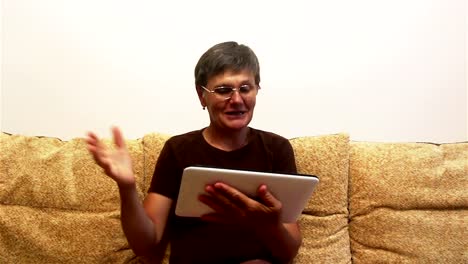 Eine-attraktive-erwachsene-Frau-ist-Video-Chat-mit-ihrer-Familie,-auf-einem-Tablet-PC,-sitzen-auf-einem-Sofa-zu-Hause.