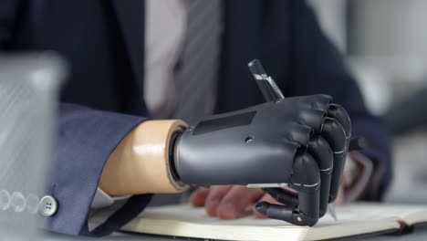 Man-with-Prosthetic-Hand-Writing-in-Notepad-at-Office-Desk