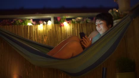 girl-in-the-evening-lies-in-a-hammock-looks-at-the-phone