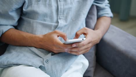 Close-up-of-male-hands-using-smartphone-touching-screen-indoors-at-home