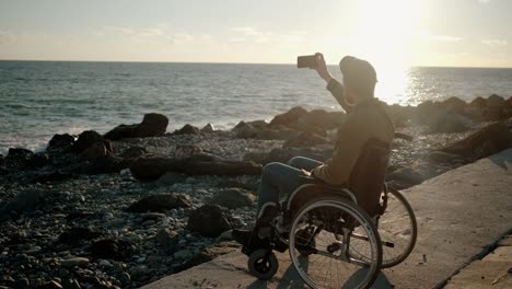 Man-is-sitting-in-invalid-carriage-taking-photos-and-video-of-sea-by-smartphone