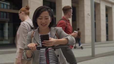 Asiatische-Frau-mit-E-Scooter-und-Smartphone