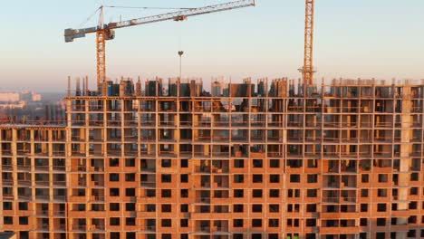 Aerial-Shot-of-the-Building-in-the-Process-of-Construction.-Labor-working-in-big-construction-site.-In-the-Background-Working-Crane-and-city