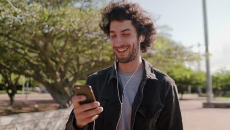 Porträt-eines-glücklichen-jungen-Mannes,-der-Musik-auf-dem-Handy-hört,-während-er-im-Park-spazieren-geht---ein-glücklicher-Mann-im-Park