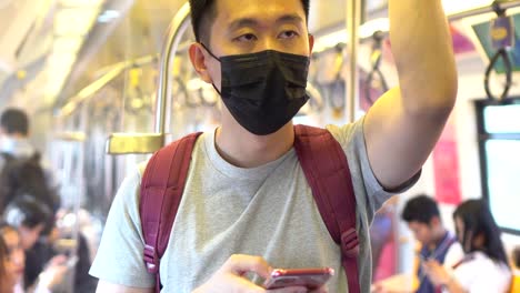 Close-up-of-one-young-Asian-man-wearing-a-black-surgical-face-mask-and-using-a-mobile-phone-in-subway-train-during-new-type-Coronavirus-Covid-19-pneumonia-outbreak-and-pm-2.5-smog-air-pollution-crisis-in-big-city