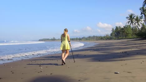 CLOSE-UP-Girl-with-crutches-walking-down-the-sandy-beach-on-tropical-island-Bali