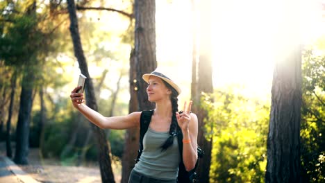 Funny-tourist-girl-in-hat-taking-selfie-photos-with-smartphone-camera-during-travelling-and-hitchhiking