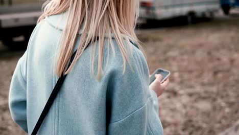 Mujer-rubia-lenta-usando-las-redes-sociales.-Vista-posterior.-Chica-surf-sitios-web-a-pie-de-calle-otoño.-Estilo-de-vida-un-disparo