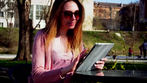 Reizendes-Mädchen-arbeiten-mit-Tablet-im-Park-und-ruht-in-Sonnenbrille