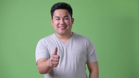 Young-handsome-overweight-Asian-man-against-green-background