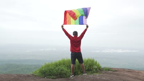 hombre-levantar-bandera-LGBTI-de-color-arco-iris-ondeando-en-duro-viento-en-el-mirador-de-alta-montaña