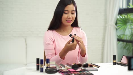 Blogger-de-belleza-actualmente-cosméticos-de-belleza-sentada-en-frente-la-cámara-para-la-grabación-de-vídeo.-Hermosa-mujer-use-cepillo-mientras-revisión-maquillaje-tutorial-transmiten-video-en-vivo-en-red-social-por-internet.