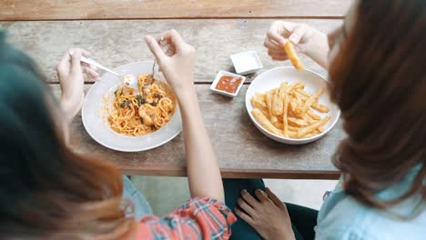 Beautiful-happy-Asian-women-lesbian-lgbt-couple-sitting-each-side-eating-a-plate-of-Italian-seafood-spaghetti-and-french-fries-at-restaurant-or-cafe-while-smiling-and-looking-at-food.