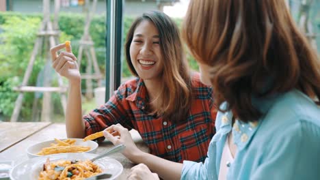 Beautiful-happy-Asian-women-lesbian-lgbt-couple-sitting-each-side-eating-a-plate-of-Italian-seafood-spaghetti-and-french-fries-at-restaurant-or-cafe-while-smiling-and-looking-at-food.