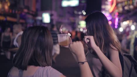 Slow-Motion---Reisende-Backpacker-asiatische-Frauen-Lesben-LGBT-Paare-tanzen-zusammen.-Weibliche-Alkohol-oder-Bier-mit-Freunden-trinken-und-feiern-auf-der-Khao-San-Road-in-Bangkok,-Thailand.