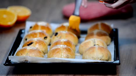 Hot-cross-buns-on-baking-tray.-Female-hands-cover-with-syrup.