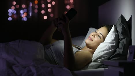 Chica-charlando-con-un-teléfono-inteligente-en-la-cama-en-la-noche