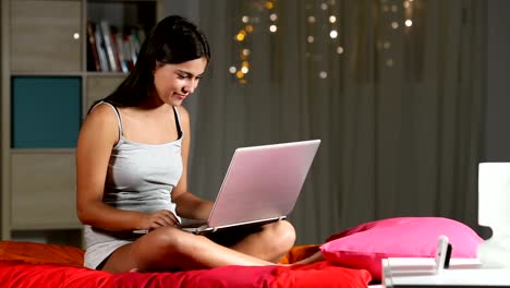 Happy-Teen-Suche-in-einem-Laptop-in-der-Nacht-auf-einem-Bett