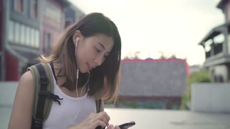 Asian-backpacker-blogger-woman-using-smartphone-for-chat,-check-social-media-and-listen-to-music-while-traveling-at-Chinatown-in-Beijing,-China.-Lifestyle-backpack-tourist-travel-holiday-concept.