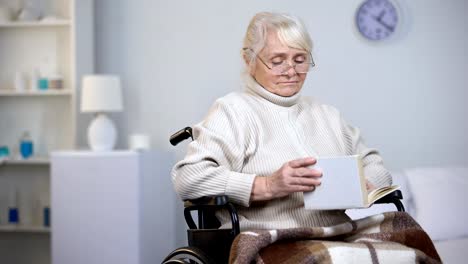 Upset-handicapped-woman-wearing-eyeglasses-reading-book,-loneliness-in-old-age