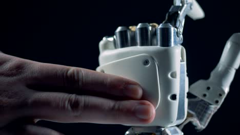 Close-up-of-human-fingers-touching-a-bionic-hand-and-making-it-move