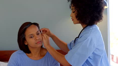 Mixed-race-female-doctor-inserting-a-hearing-aid-machine-on-womans-ear-at-home-4k