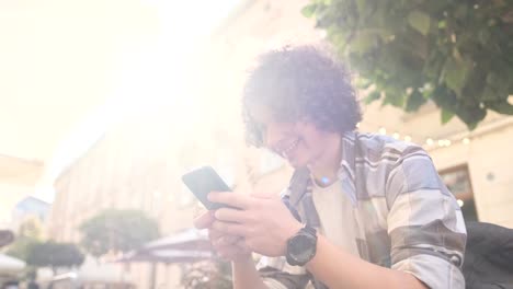 Guapo-joven,-turista-o-estudiante,-Millennial-en-traje-hipster,-utilizando-su-smartphone-se-desplaza-a-través-de-las-redes-sociales-de-alimentación-en-el-dispositivo,-comprobando-mapa-o-leer-noticias-en-la-aplicación,-mirando-a-su-alrededor,-al-aire-lib