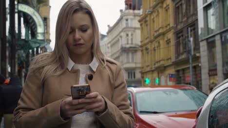 Eine-junge-schöne-Frau-arbeitet-an-einem-Herbsttag-auf-einem-Smartphone-in-einer-Straße