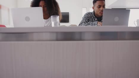 Black-teenage-brother-and-sister-sitting-at-home-using-laptop-computers,-front-view,-tilt-shot