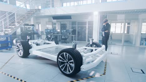 Automotive-Engineer-Working-on-Electric-Car-Chassis-Platform,-Using-Augmented-Reality-Headset.-In-Innovation-Laboratory-Facility-Concept-Vehicle-Frame-Includes-Wheels,-Suspension,-Engine-and-Battery.