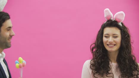 The-young-girl-stands-on-a-pink-background.-She-approaches-a-man-and-gives-decorative-multicolored-eggs.-During-this-he-kisses-her.-Sincerely-smile.