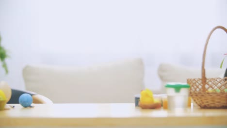 Little-playing-boy-with-bunny-ears-on-his-head-is-hiding-under-the-wooden-table,-full-of-Easter-decorations.-Boy-is-playing-with-Easter-bunnies-on-the-table,-hiding-his-face.