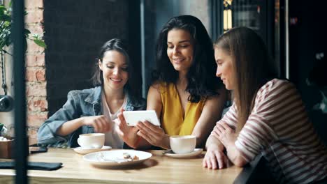 Group-of-young-women-watching-smartphone-screen-laughing-drinking-coffee-in-cafe