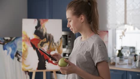 Female-Painter-Eating-Apple-and-Using-Smartphone