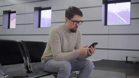 El-hombre-está-mirando-en-la-pantalla-del-teléfono-móvil-sentado-en-la-silla