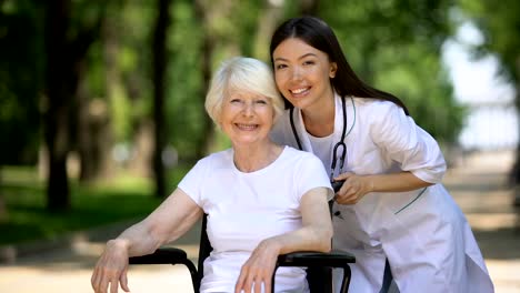 Nurse-and-old-handicapped-woman-smiling-at-camera-and-showing-thumbs-up-gesture