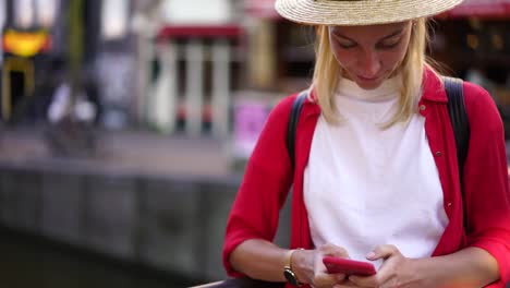 Viajero-femenino-positivo-en-sombrero-usando-el-teléfono-móvil-para-chatear-en-línea-en-itinerancia