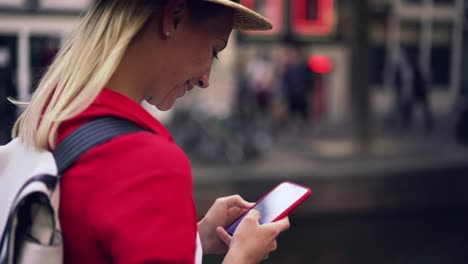 Vista-lateral-de-cerca-del-cabello-rubio-mujer-caucásica-caminando-al-aire-libre-con-el-teléfono-móvil-en-las-manos