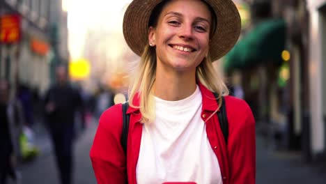 Close-up-portrait-of-authentic-Caucasian-female-standing-with-smartphone-in-hands-and-sincerely-laughing-on-camera