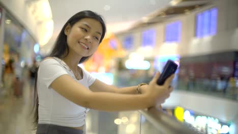 Lächelnde-asiatische-Frau-macht-Selfie-in-Einkaufszentrum