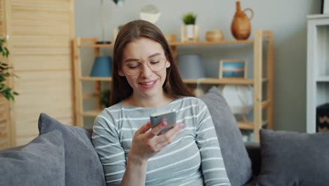 Attractive-student-using-smartphone-leaving-voice-message-smiling-at-home