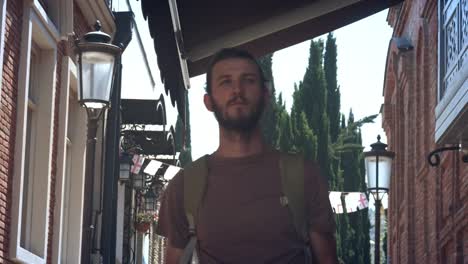 Young-guy-traveler-is-walking-in-a-European-city-with-a-map-in-his-hands.-A-tourist-is-looking-for-a-way-or-lost.-Sightseeing-in-the-new-city.-Man-traveler-reading-geographical-atlas