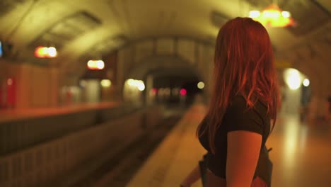 Hermosa-mujer-fresca-con-pecas,-piercings-y-pelo-rojo-mirando-el-teléfono-inteligente-en-la-estación-de-metro,-durante-el-verano-soleado-en-París.-Fondo-subterráneo-borroso.-4K-UHD.