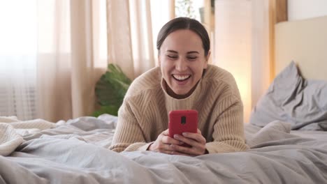 Mujer-teniendo-mensajes-de-texto-divertidos-en-el-teléfono-móvil-en-la-cama