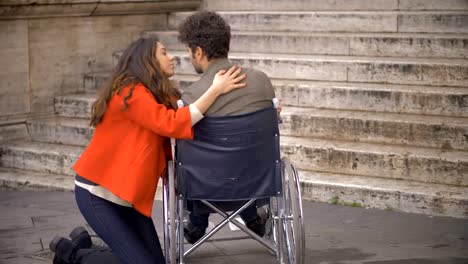 Young-woman-hugging-her-sad-boyfriend-in-wheelchair-in-the-city.love,-empathy