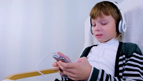 Boy-hört-Musik-in-Kopfhörern-im-Smartphone-und-singt-zu-Hause-im-Sessel-sitzend.