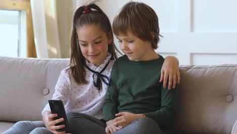 Dos-niños-niña-aprendiendo-usando-el-teléfono-inteligente-juntos-en-el-sofá