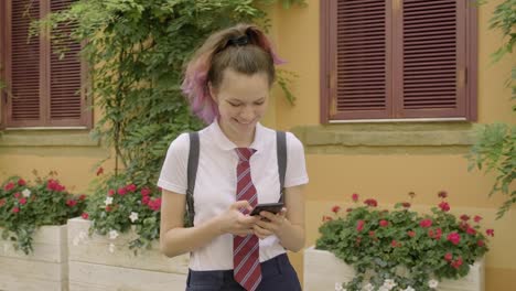 Hermosa-estudiante-adolescente-chica-con-teléfono-inteligente-leer-y-escribir-mensaje-de-texto,-sonriendo-en-la-calle-de-la-ciudad