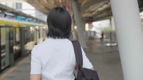 Retrato-de-mujer-asiática-con-auriculares-escuchando-música-y-usando-teléfono-inteligente-para-chatear-con-amigos-o-navegar-mientras-espera-un-tren.-Tecnología-en-la-vida-cotidiana-y-los-viajes.