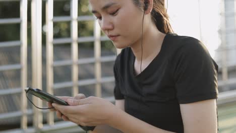 Attractive-caucasian-woman-athlete-running-using-mobile-texting-sharing-messages-on-social-media-communication-while-sitting-beside-the-street-in-urban-city-sunset.